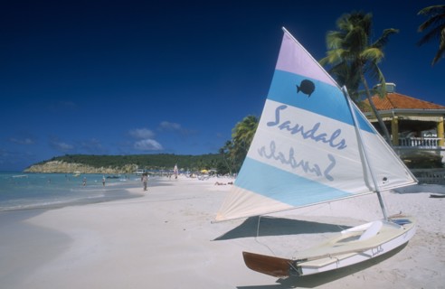 WEST INDIES, Antigua, Dickenson Bay, View along sandy beach lined with palms with boat in the