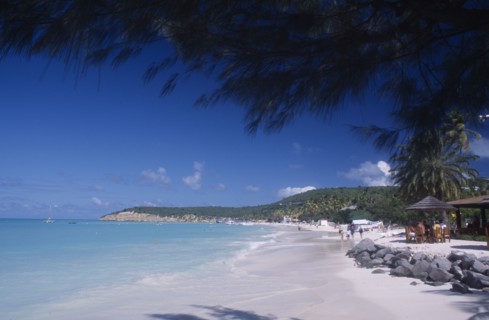 WEST INDIES, Antigua, Dickenson Bay, View along beach towards tree covered headland with people