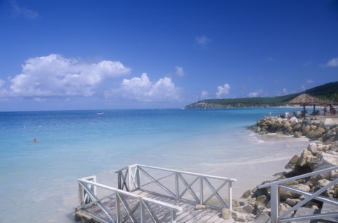 WEST INDIES, Antigua, Dickenson Bay, Raised area of sand fortified by rocks with people sitting on