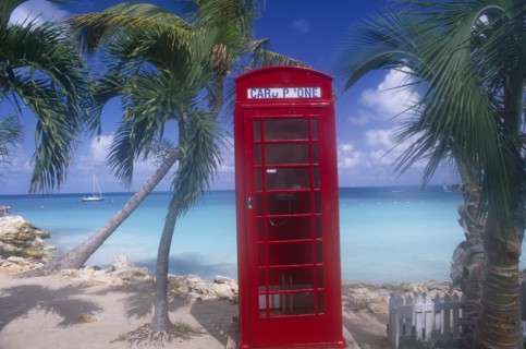 WEST INDIES, Antigua, Dickenson Bay, Red telephone box on sand surrounded by palm trees with sea