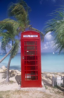 WEST INDIES, Antigua, Dickenson Bay, Red telephone box on sand surrounded by palm trees with sea