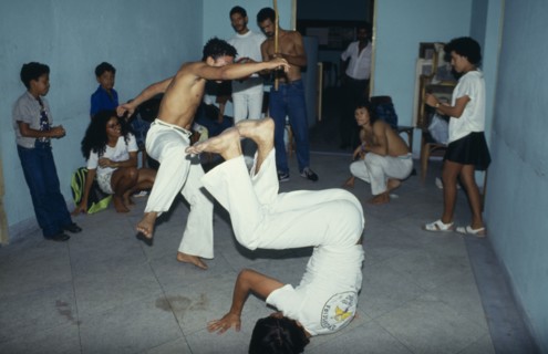 20018911 BRAZIL  Capoeira Local men in animated poses of martial arts  inside a small room with spectators.