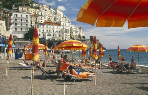 ITALY, Campania, Amalfi Coast, Amalfi.  Beach with sunbathers on loungers under yellow and orange