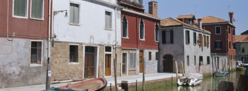 ITALY, Veneto, Venice, Murano Island.  View along canalside houses with boats moored to posts in