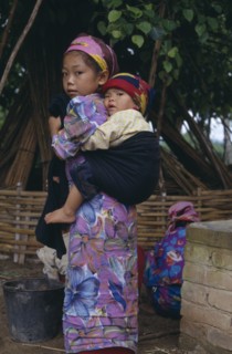 CHINA, Yunnan Province, Menghun, Dai girl carrying child on her back.