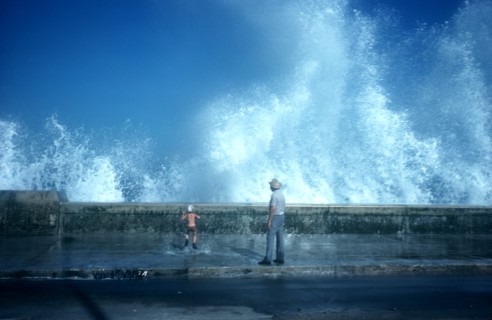 CUBA, Havana, Malecon, Old man and small boy standing on pavement with waves crashing over the sea