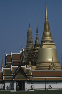 THAILAND, Bangkok, Grand Palace, Aka Wat Phra Kaeo. Exterior view of golden spires and man on guard