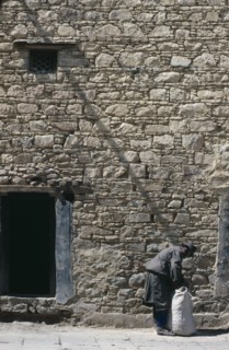 CHINA, Tibet, Lhasa, Man tying sack in the street beside a stone building