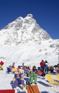 ITALY, Valle d’Aosta, Breuil Cervina, Group of skiers sunbathing at the foot of the Matterhorn.