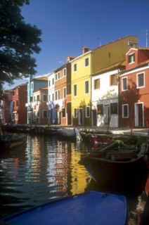 ITALY, Veneto, Venice, Burano Island.  Boats moored at canal-side overlooked by row  of brightly
