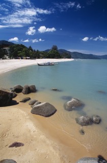 MALAYSIA, Penang, Batu Ferringhi, View along shore of quiet sandy beach with moored boat in middle