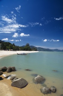 MALAYSIA, Penang, Batu Ferringhi, View along shore of quiet sandy beach with moored boat in middle