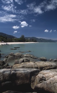 MALAYSIA, Penang, Batu Ferringhi, View over rocks and bay of turquoise water towards distant moored