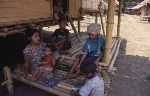 THAILAND, North, Mae Sai , Karen refugee mother feeding child with four other children sitting in