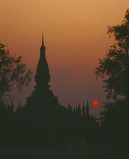 LAOS, Vientiane, Pha That Luang Sacred Stupa silhouetted against red setting sun and orange sky.
