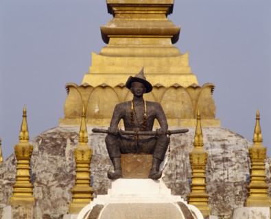 LAOS, Vientiane, Pha That Luang Sacred Stupa with statue of King Setthathirat in foreground.