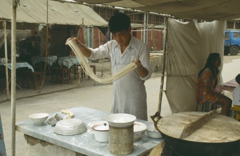 CHINA, Henan Province, Shaolin Monastery, Young man making noodles at food stall by swinging the