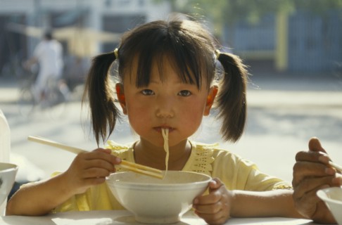 CHINA, Guizhou, Guiyang, Pony tailed young girl eating noodles from bowl with chopsticks