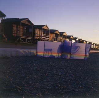 ENGLAND, Kent, Whitstable, Couple silhouetted behind a wind break on the beach in front of wooden