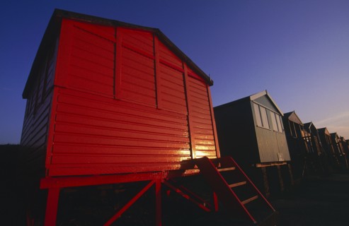 ENGLAND, Kent, Whitstable, Row of beach huts painted different colours on the beach in golden