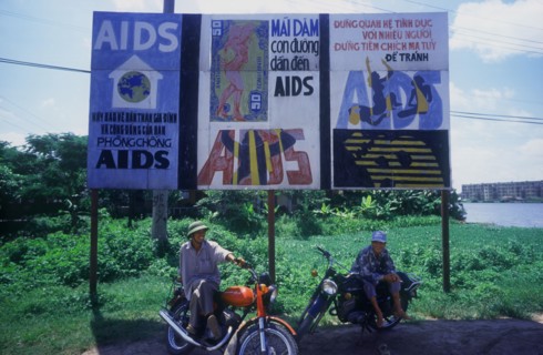 VIETNAM, Hai Duong, Two young men sitting on their motorcycles under a billboard of aids awareness