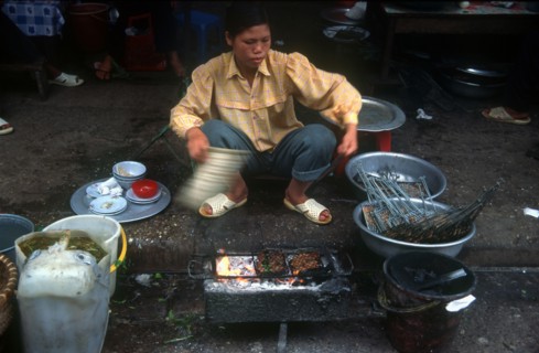 VIETNAM, Hanoi, Woman cooking at curb side food stand.
