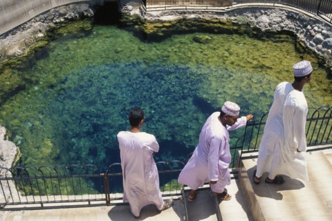 OMAN, Al Rustaq, "Three men in traditional white dishdashas and brimless, circular hats standing