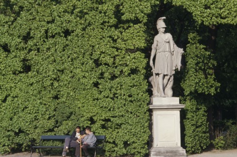 AUSTRIA, Vienna, Schonbrunn Gardens.  Classical statue against hedge with two visitors sitting on
