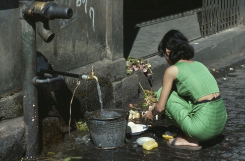 MYANMAR, Yangon, Young woman using tap in street to wash dishes in the market.