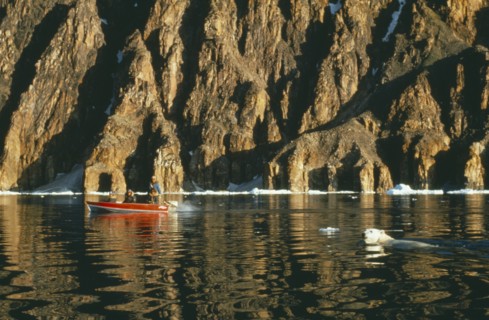 CANADA, Baffin Island, Eskimos in motor boat and Polar Bear fishing in water against a backdrop of