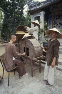 VIETNAM, Hue, Monks husking rice in a traditional hand driven machine