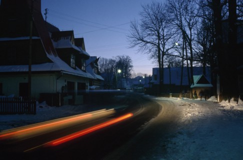 POLAND, Zakopane, Chocholow, Streaked red car lights in motion blur on road through snowy village