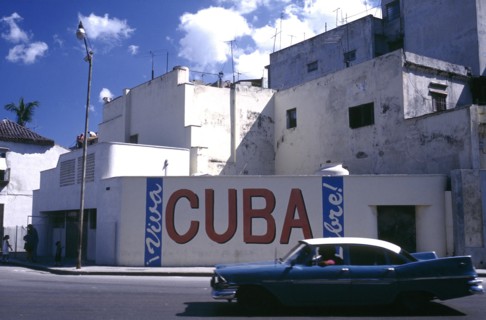 CUBA, Havana, Street scene with passing classic car and the words Viva Cuba painted on the wall