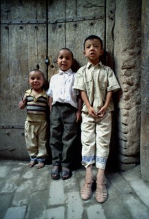 CHINA, Xinjiang, Kashgar, Three young boys standing against a wooden door on a cobbled street