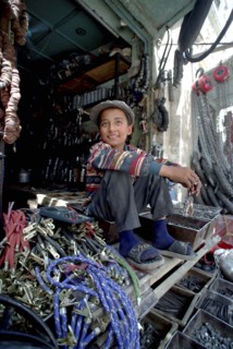 CHINA, Xinjiang, Kashgar, Young hardware vendor sitting amongst goods for sale