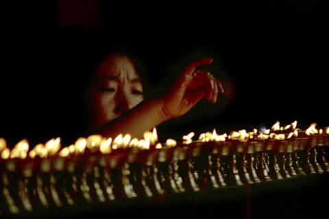 CHINA, Tibet, Lhasa, Jokhang Temple. Woman lighting prayer lamps fueled with Yak butter