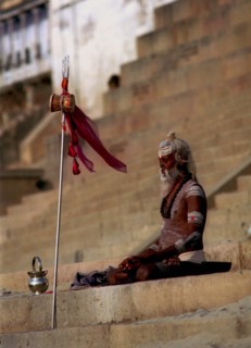 INDIA, Uttar Pradesh, Varanasi, Sadhu meditating in the early morning sun on the ghats of the River