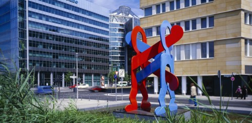 GERMANY, Berlin, Red and blue sculpture by Keith Haring entitled Boxers with city road and