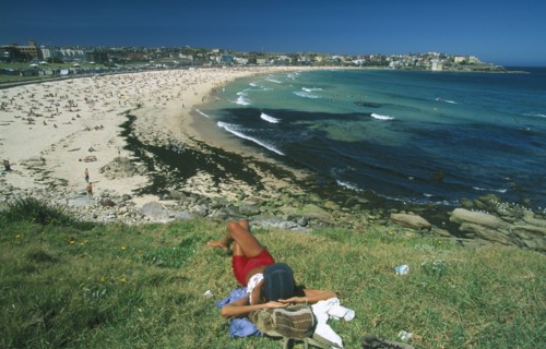 AUSTRALIA, New South Wales, Sydney, View over Bondi beach with woman sunbathing in the foreground