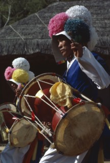 SOUTH KOREA, Arts, Dance, Farmers Dance.  Young man wearing paper flowered hat and playing drum.