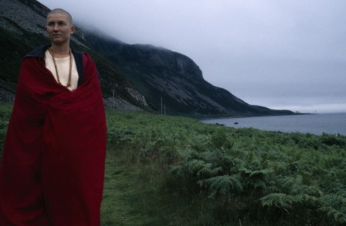SCOTLAND, Clyde, Tibetan Nun draped in a red robe standing next to coastline by green landscape and