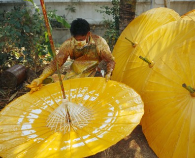 THAILAND, Chiang Mai Province, Bo Sang Village, Man spinning cotton umbrella as he applies colour