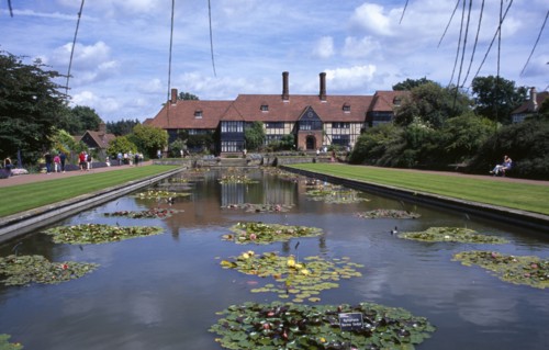20059213 ENGLAND Surrey Woking Wisley Royal Horticultural Society Garden. View across formal pond with water lilies towards the Tudor style half timbered main entrance building.
