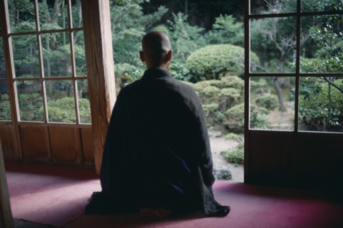 JAPAN, Buddhism, Zen Buddhist monk meditating in front of screen open to garden.