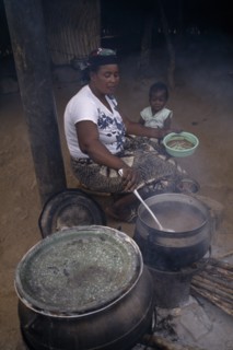 GHANA, Cherepani, Woman cooking over wood burning open topped stove and passing helping of food to