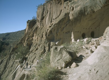 USA, New Mexico, Bandelier National Monument. , Visitors climbing ladder up a cliff towards the
