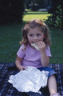 ENGLAND, West Sussex, Chichester, The Bishops Palace Gardens.  Girl aged three eating brown bread