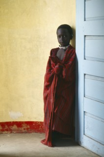TANZANIA, Ngorongoro, Masai child standing between yellow wall and blue door.  The Masai have been