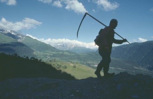 GEORGIA, Caucasus Mountains, Silhouetted figure of man carrying scythe with mountain backdrop.
