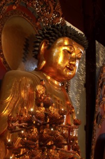 CHINA, Shanghai, Jade Buddha Temple. Golden Buddha statue with seated Buddha candle stand in front